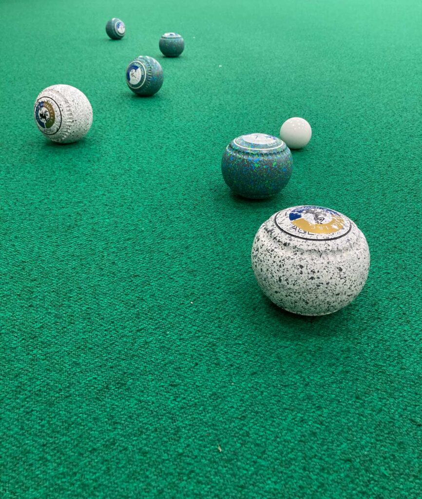 Four green lawn bowls and two white bowls close to a white jack